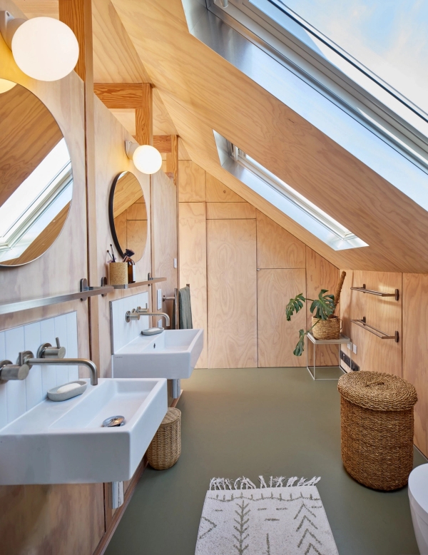 Loft converter bathroom featuring dual white pedestal sinks, round mirrors, skylights, and olive green rubber flooring, Love Locations E17.