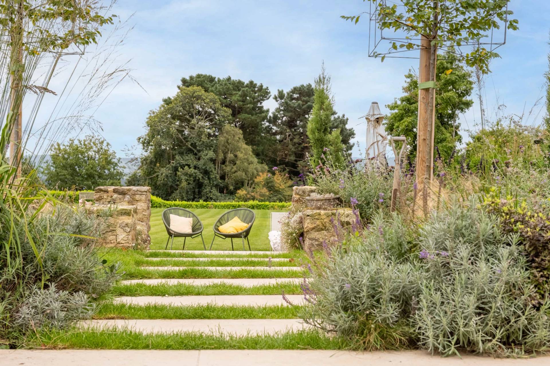 Terraced garden lawn with stone retaining walls and stepping stones overlooking rolling countryside, Love Locations GU28.