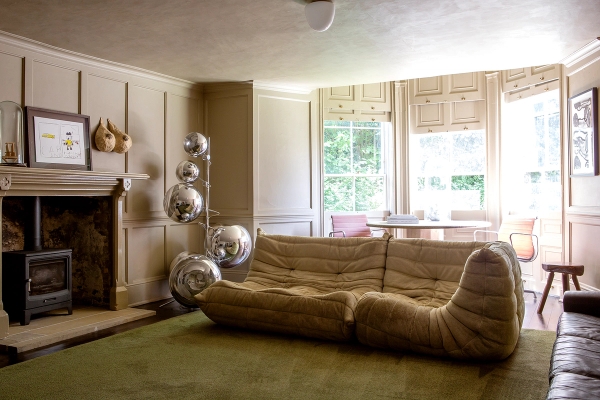 Eclectic lounge room with a tan velvet wave sofa, green carpet floor, and mirrored sphere sculptures, Love Locations ME13.