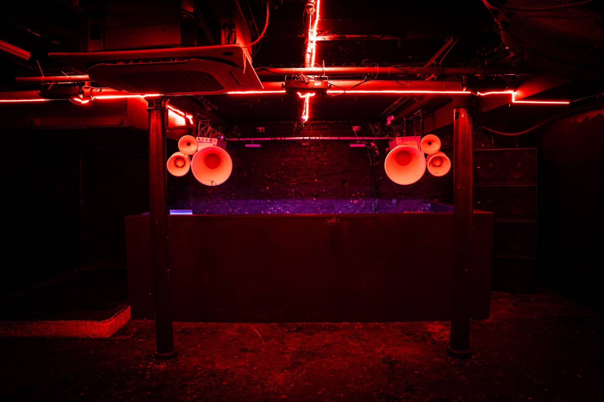 Frontal view of a DJ performance stage and horn speaker stacks under red LED tubes in Manchester M3 via Love Locations.