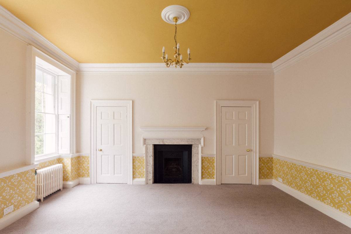Grand bedroom featuring ochre yellow ceiling trim and wallpaper, twin sash windows, and white double closet doors, Love Locations.