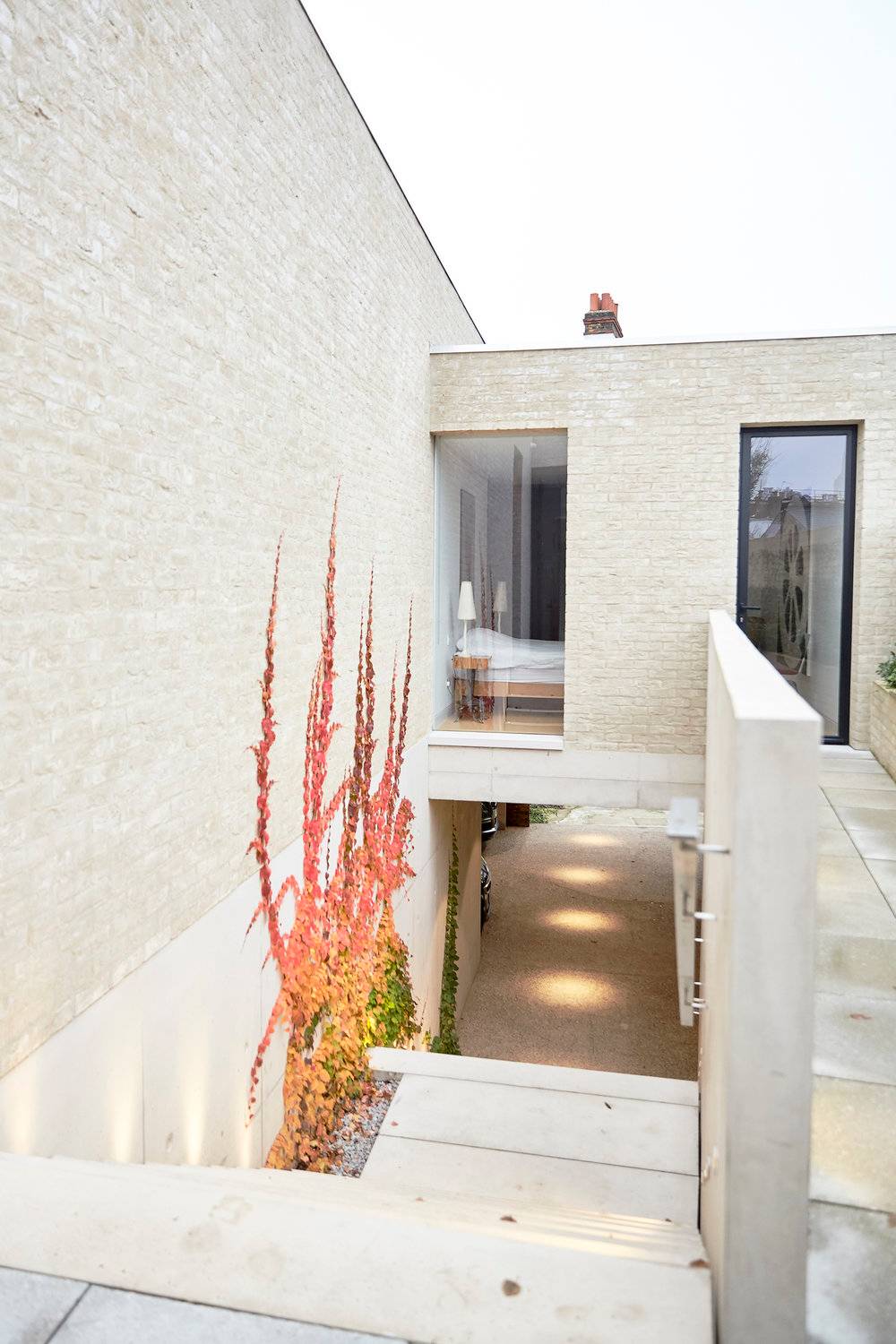 High-angle view into a multi-level subterranean concrete lightwell courtyard with modern brick cladding and lush red plants, ideal for high-concept fashion photography, Love Locations SW8.