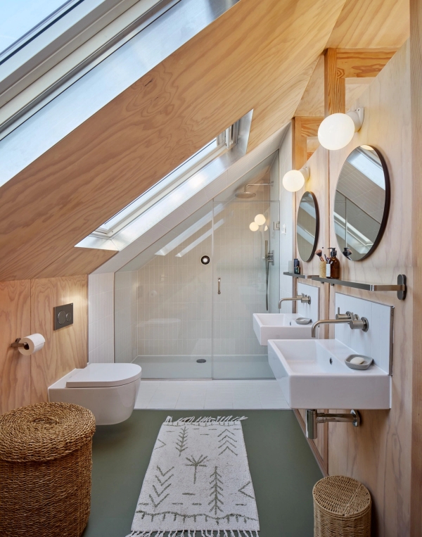 Attic loft bathroom under sloped ceilings with dual skylights, walk-in shower, and white pedestal sinks, Love Locations E17.