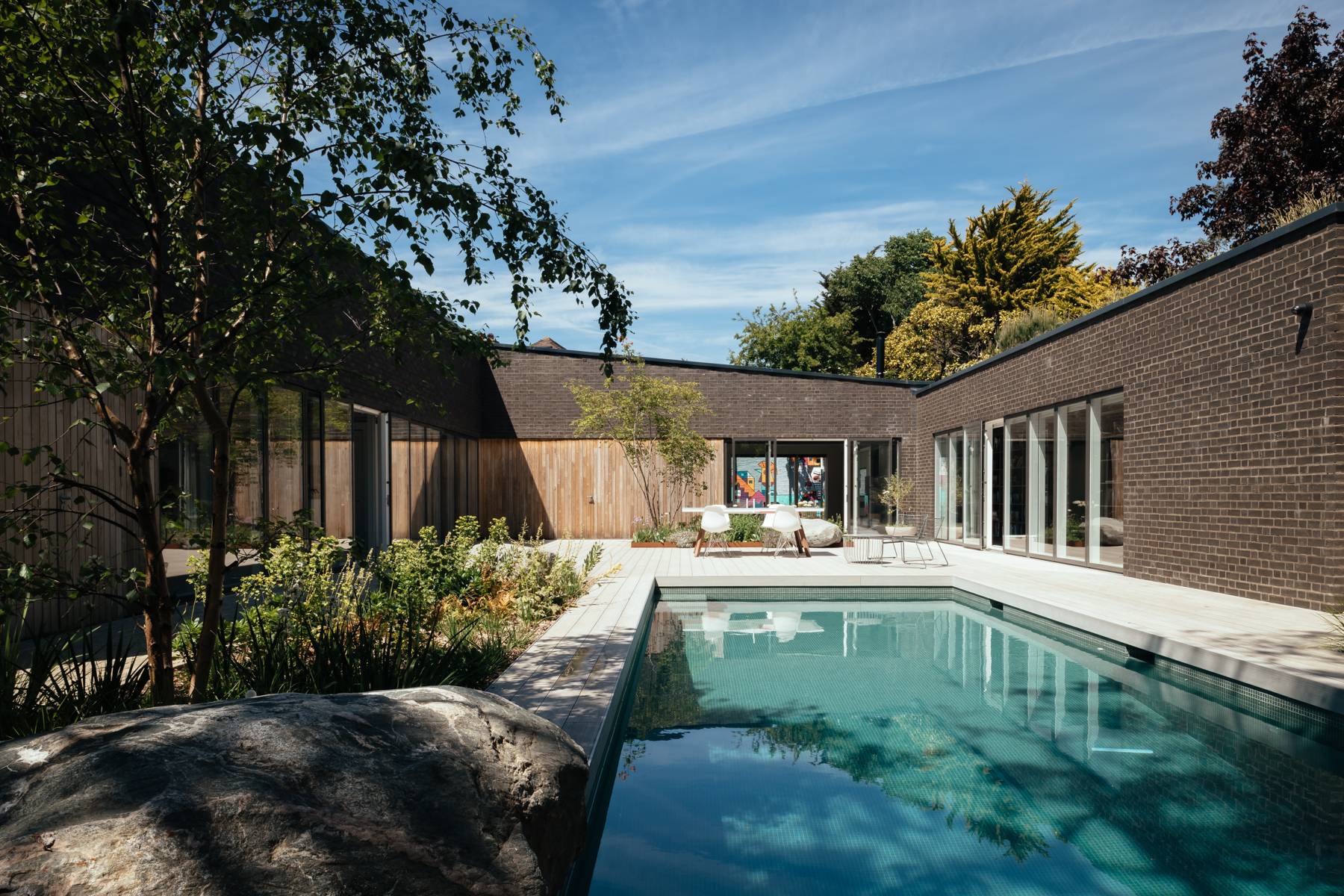 Courtyard swimming pool surrounded by dark timber decking, mature trees, and modern architecture, Love Locations BN3.