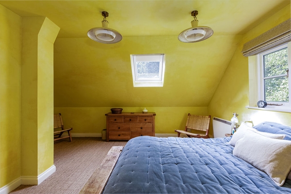 Bright loft bedroom with skylight and mustard walls at Love Locations house location in Liss, Hampshire GU33.