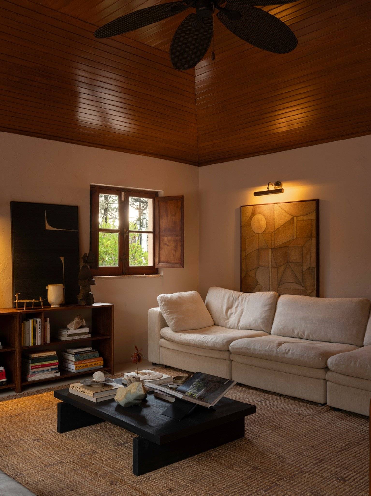 Cozy sitting room with white sofa, dark timber coffee table, small shuttered window, and warm lighting, Love Locations 2705-064.