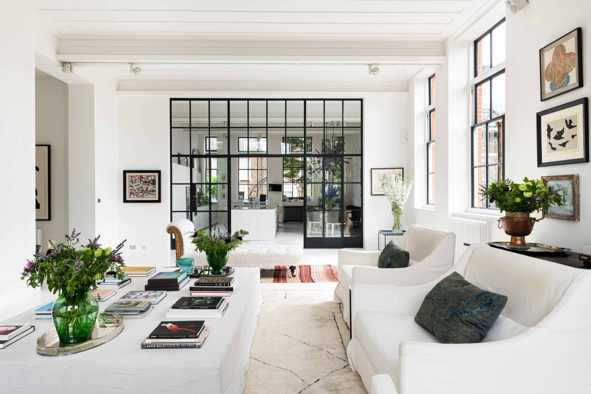 Wide-angle perspective of a white industrial living space with black metal Crittall glass partition walls and plush white seating, Love Locations.
