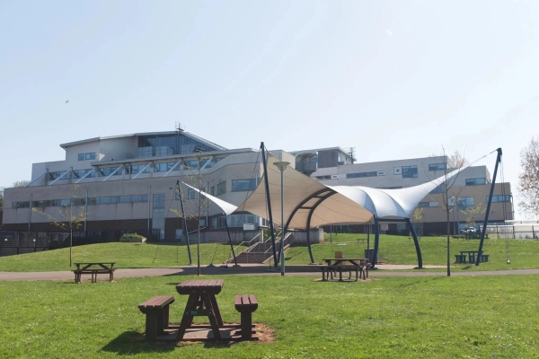 Love Locations open school playground location BS7: Outdoor recreational area featuring wooden picnic tables and a tensile fabric sun canopy shade, tailored for lunch break scenes and student lifestyle shoots.