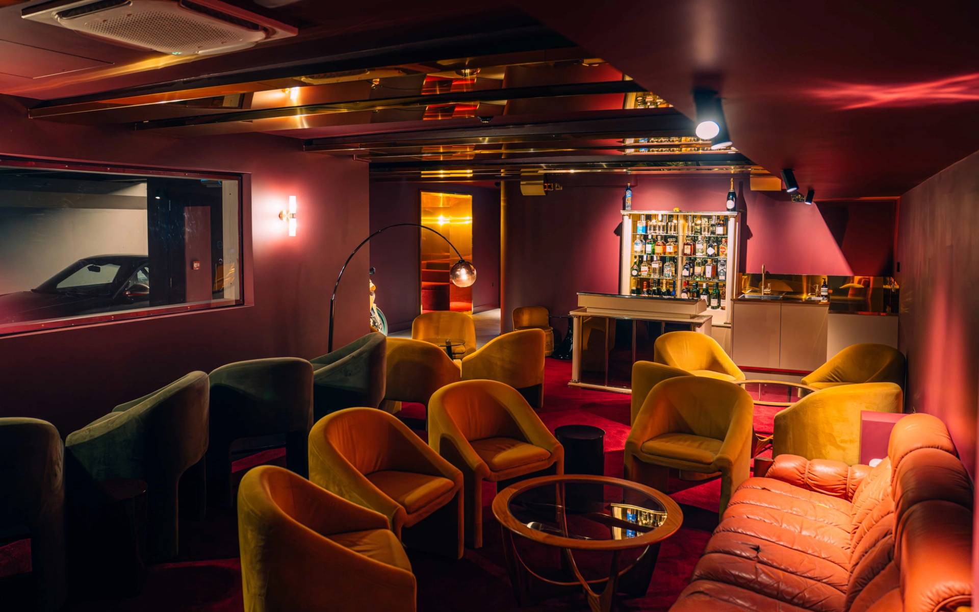 Atmospheric speakeasy cocktail bar shoot venue featuring mustard velvet chairs, brass accents, and a backlit liquor display via Love Locations.