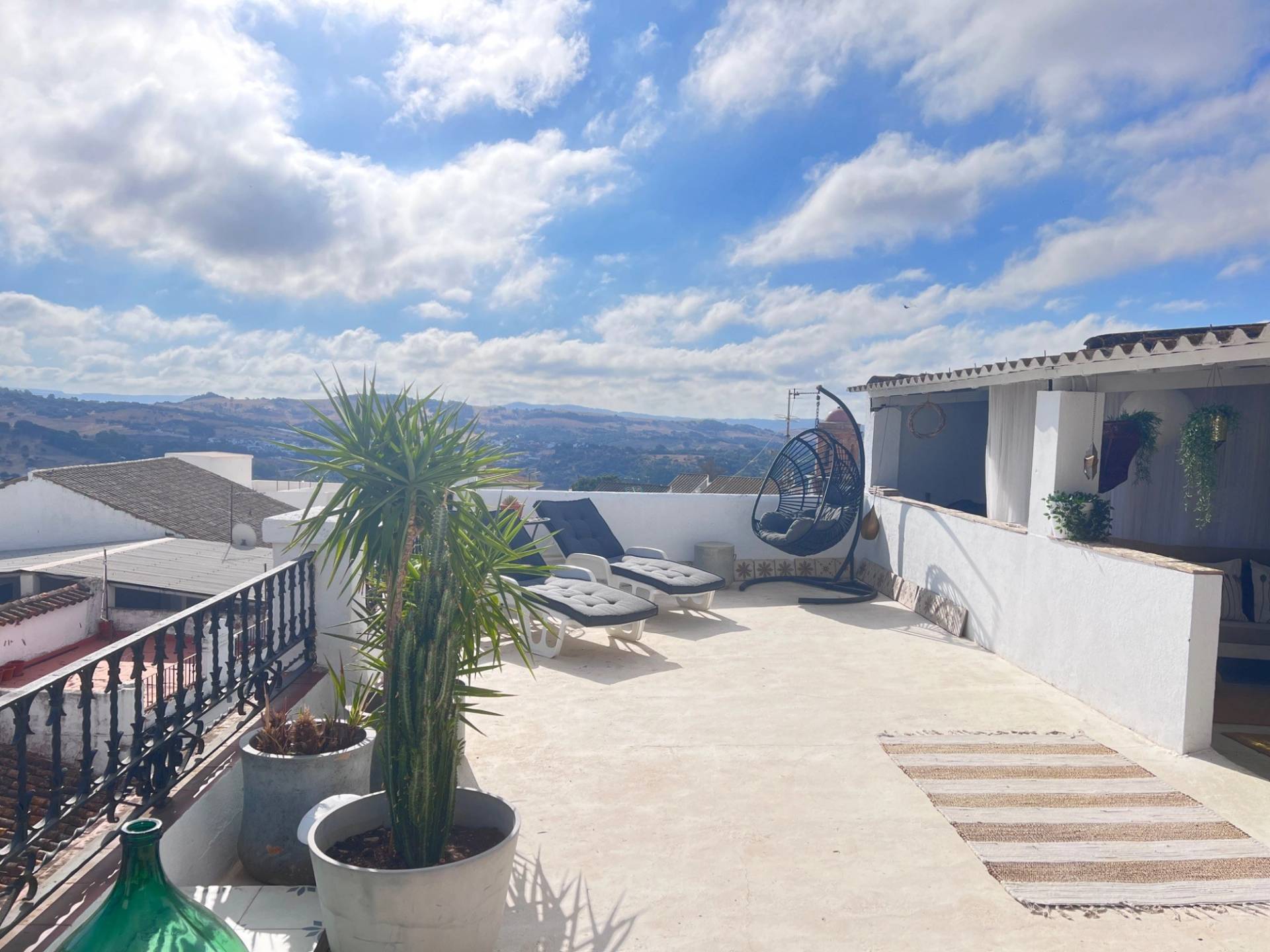 Sunlit rooftop terrace location house in Jimena de la Frontera Cádiz from Love Locations, featuring potted tropical plants, outdoor lounge seating, and panoramic mountain views.