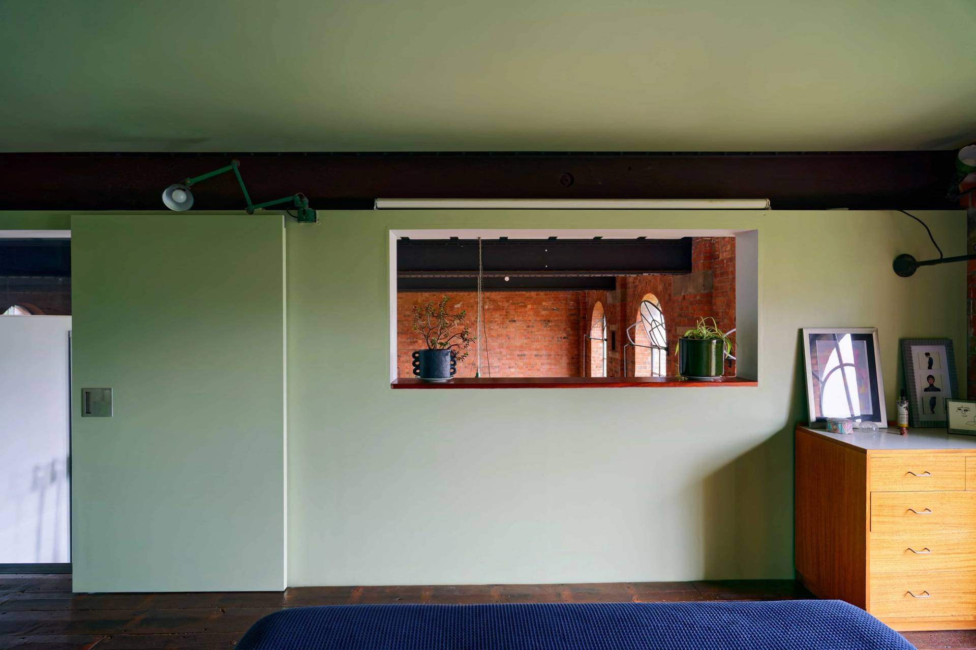 View through an internal cutout wall window looking into an exposed brick warehouse lounge room, Love Locations E14.