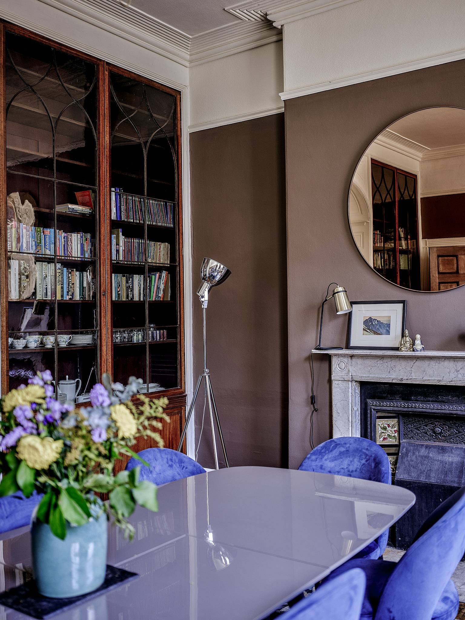 Taupe dining room view with blue velvet chairs, large round wall mirror, and glass cabinet, Love Locations.