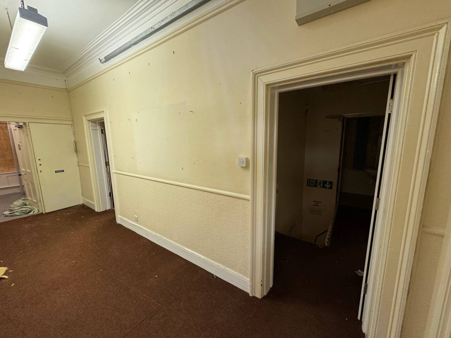 Empty institutional hallway with cream walls and dark brown carpet inside an unmodernised mansion property, via Love Locations.