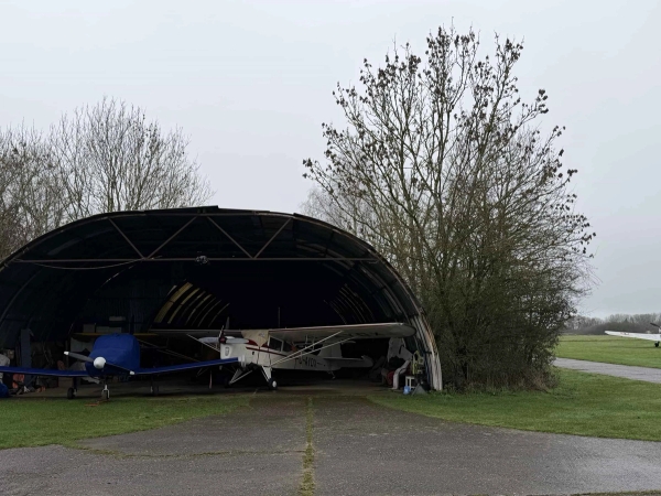 Large curved aircraft hangar housing a parked plane on a historic airfield site, ideal for industrial music video backdrops, Love Locations.