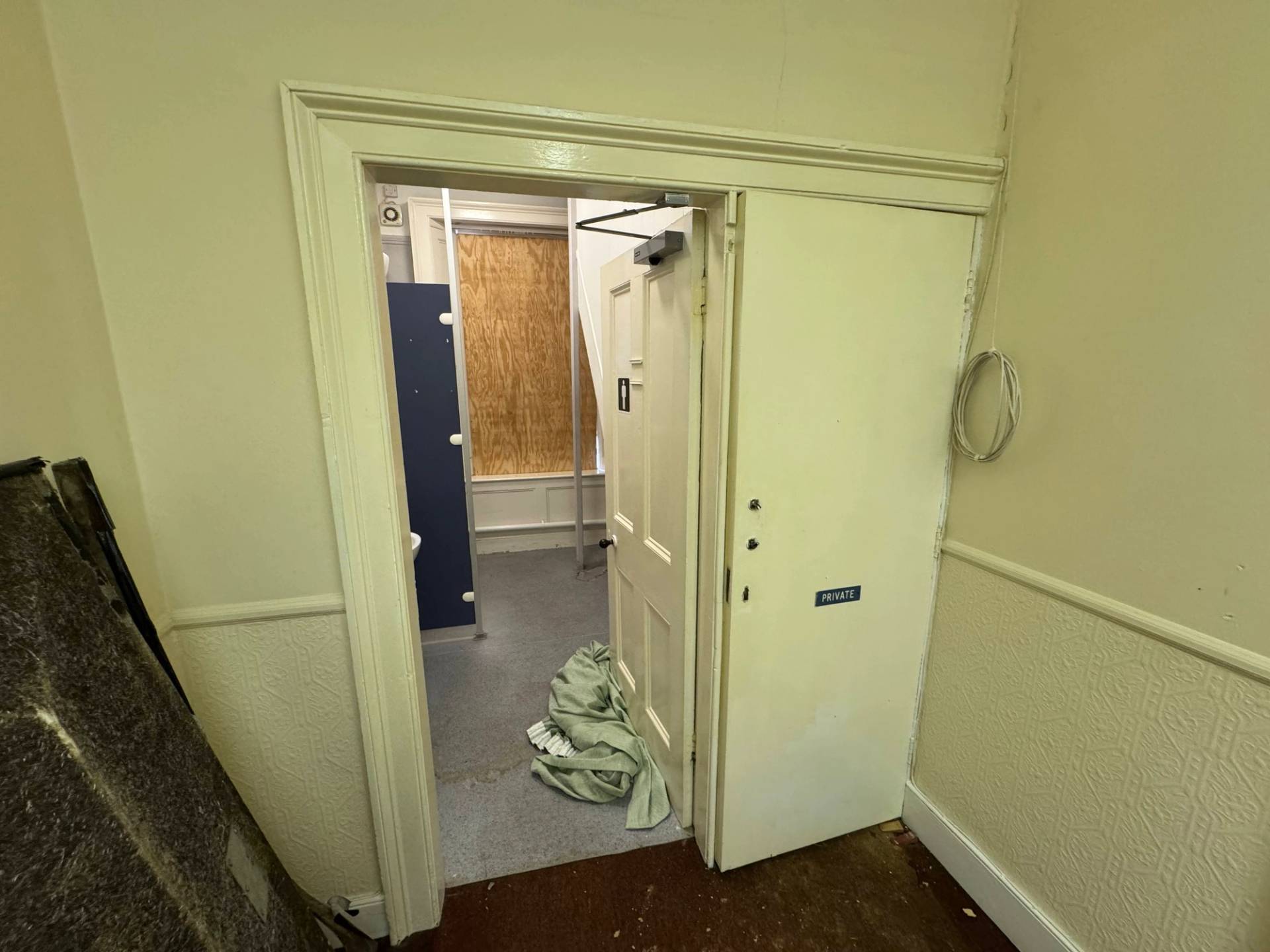 Internal doorway opening into a distressed restroom facility with blue cubicle partitions, Love Locations Nottingham.