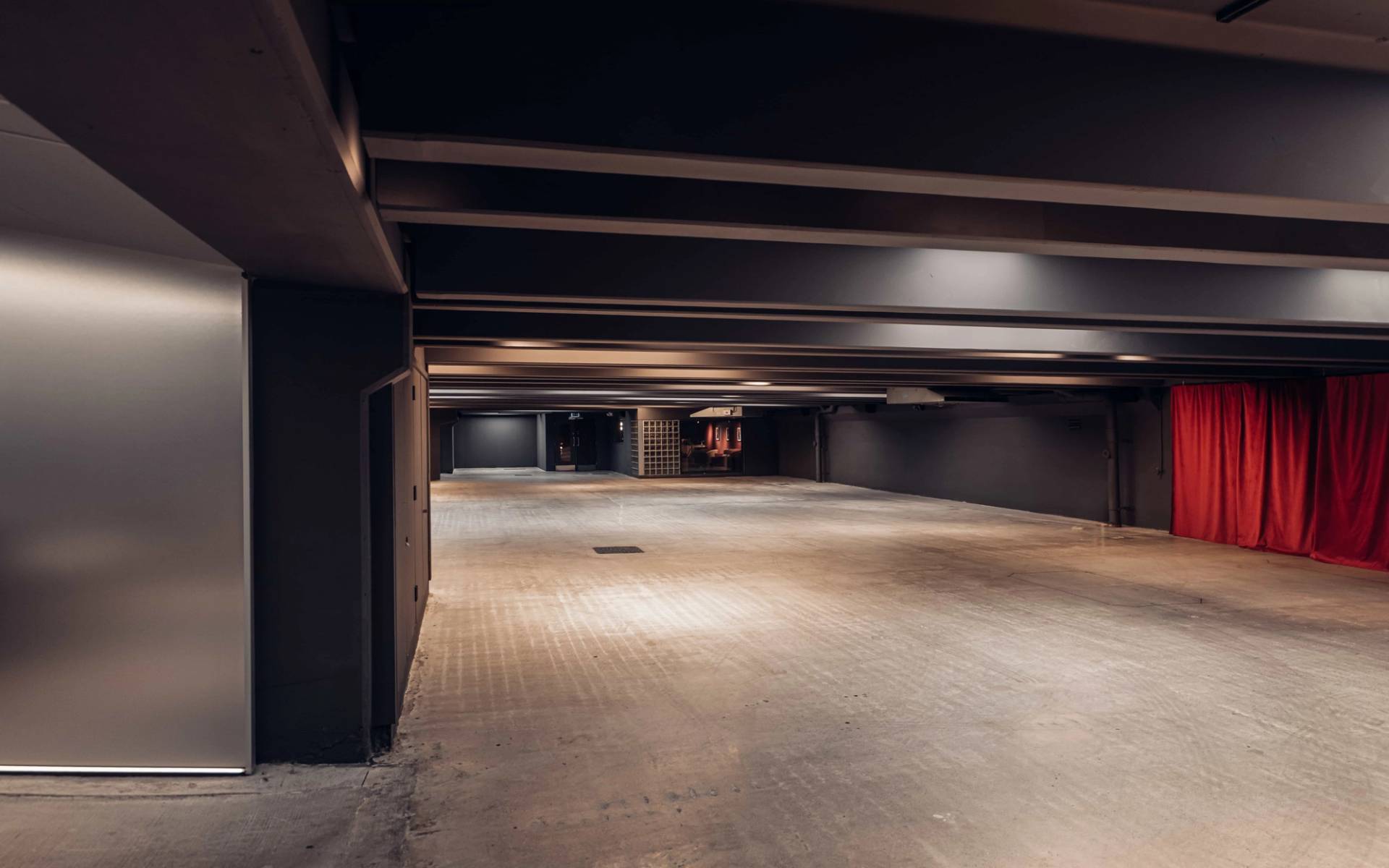 Wide perspective of a subterranean concrete basement film location in Brentford TW8 available via Love Locations, showcasing dark overhead beams and open floor space.