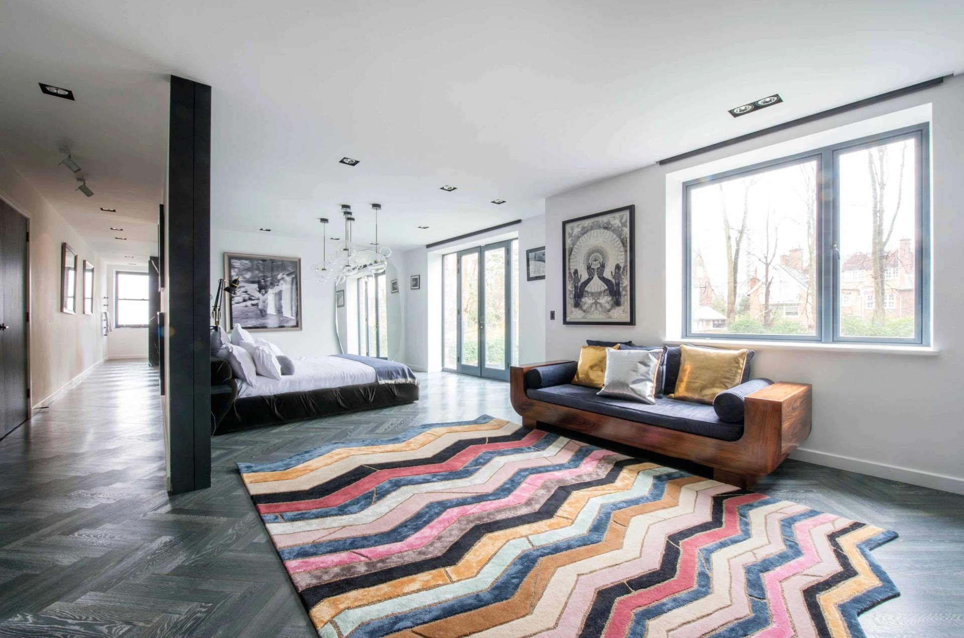 Spacious contemporary bedroom layout featuring a colorful geometric rug, low-profile seating, and access to a private balcony, Love Locations NW3.