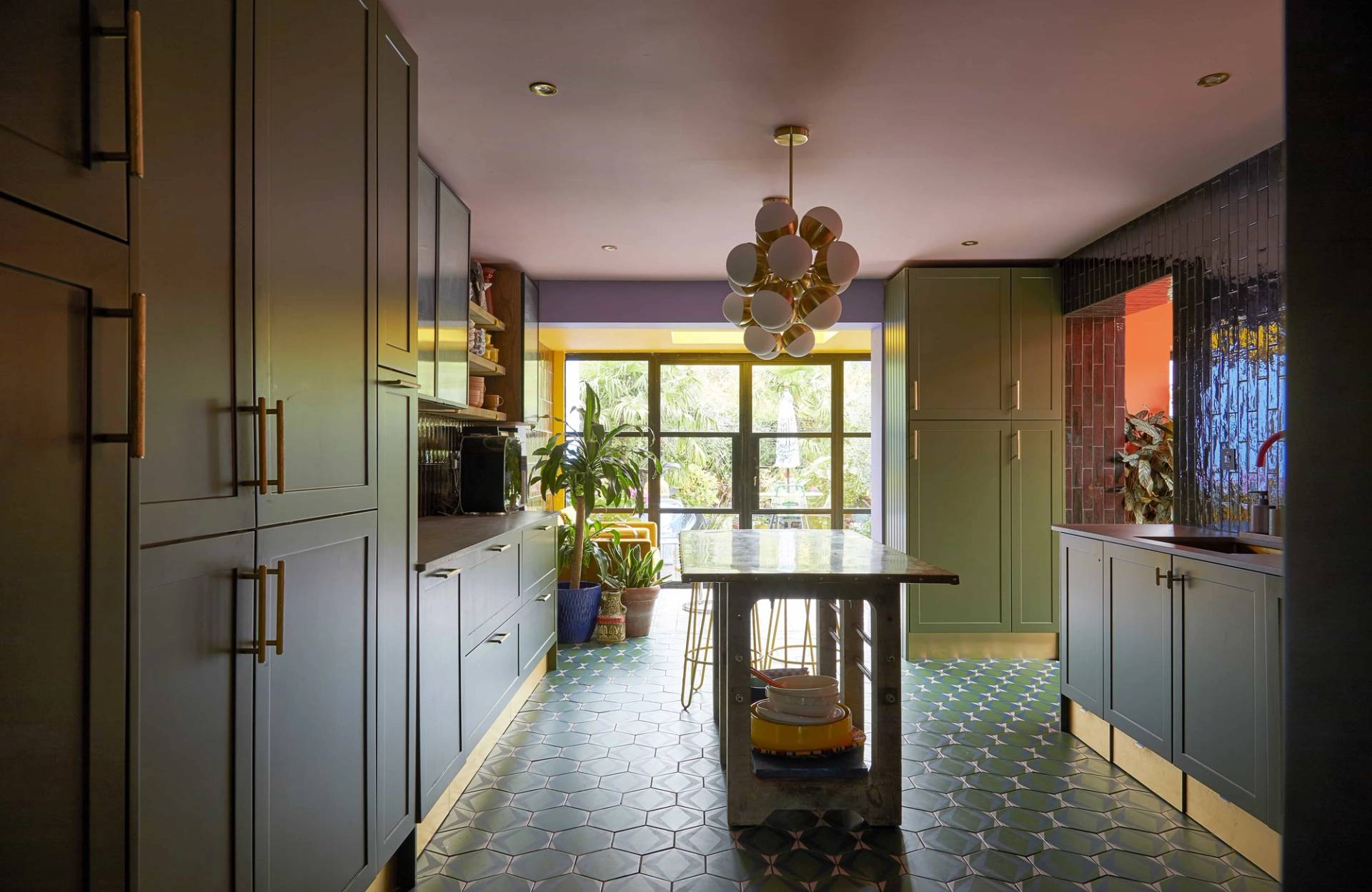 Olive green kitchen location featuring geometric green floor tiles, a mobile kitchen island, and a pink ceiling, Love Locations SE6.