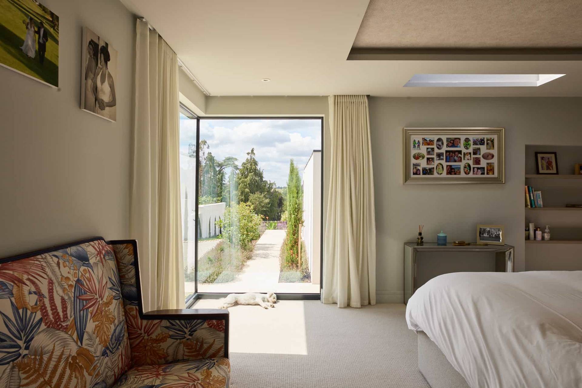 Master bedroom seating corner featuring a patterned armchair beside tall glass patio doors framing green grounds, Love Locations.