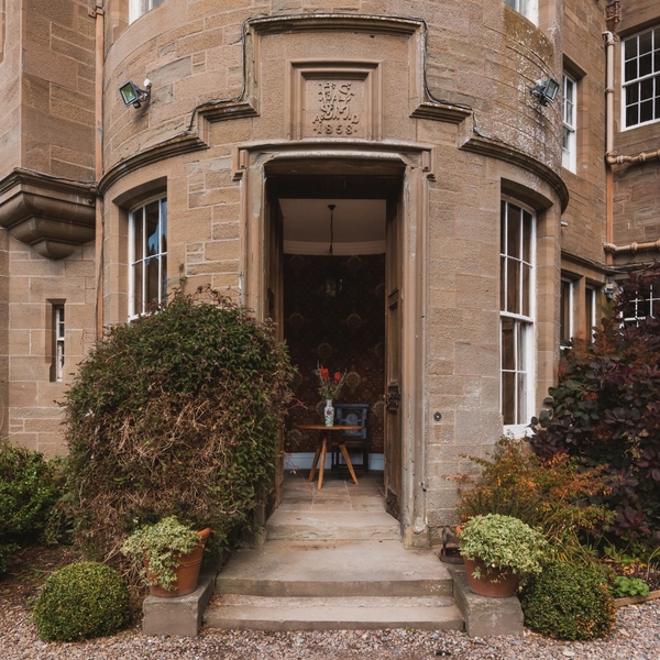 Arched stone entrance doorway of a grand Scottish castle with steps and potted plants, Love Locations KY15.