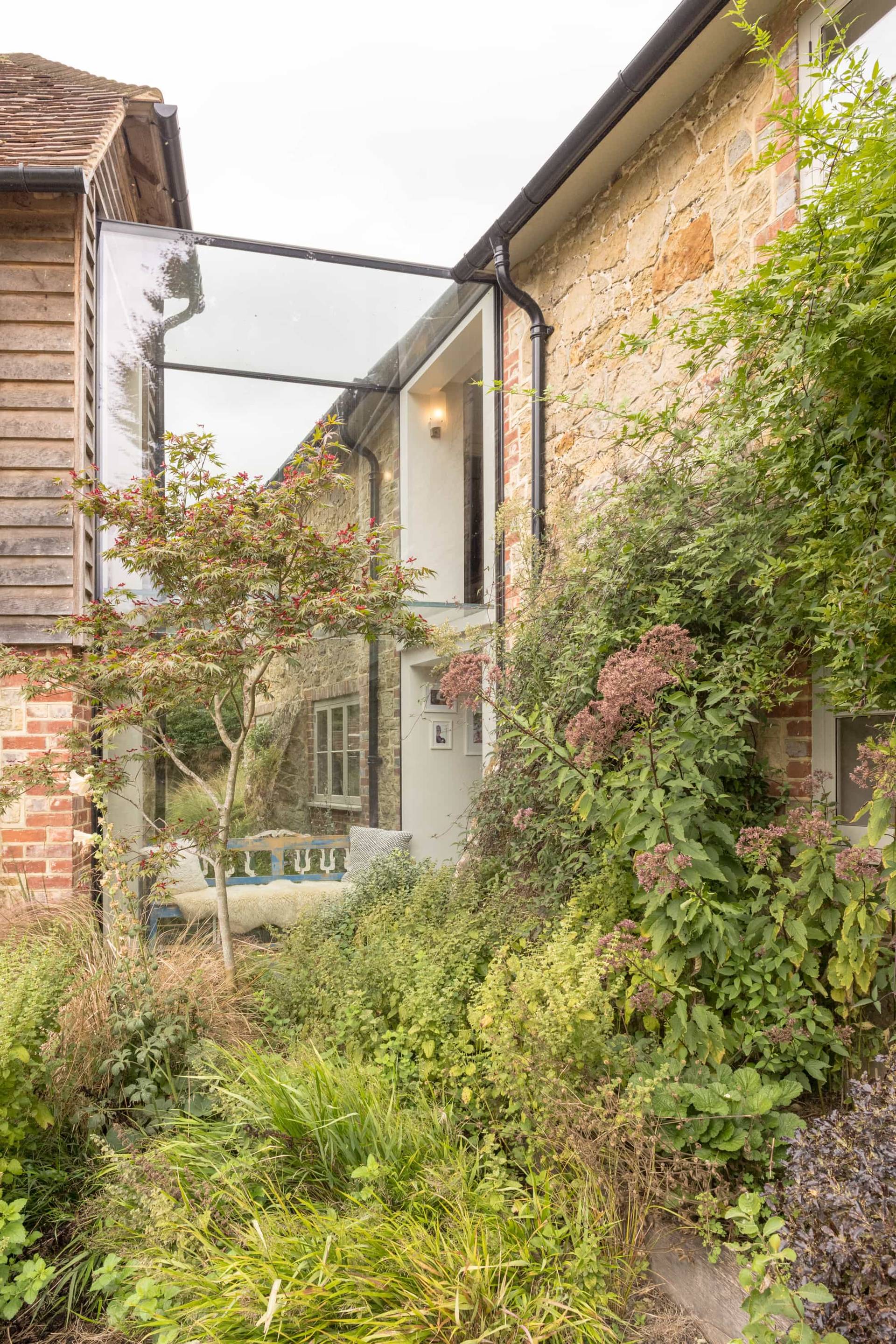 Exterior view of a glass link corridor connecting stone and timber barn buildings, Love Locations GU28.