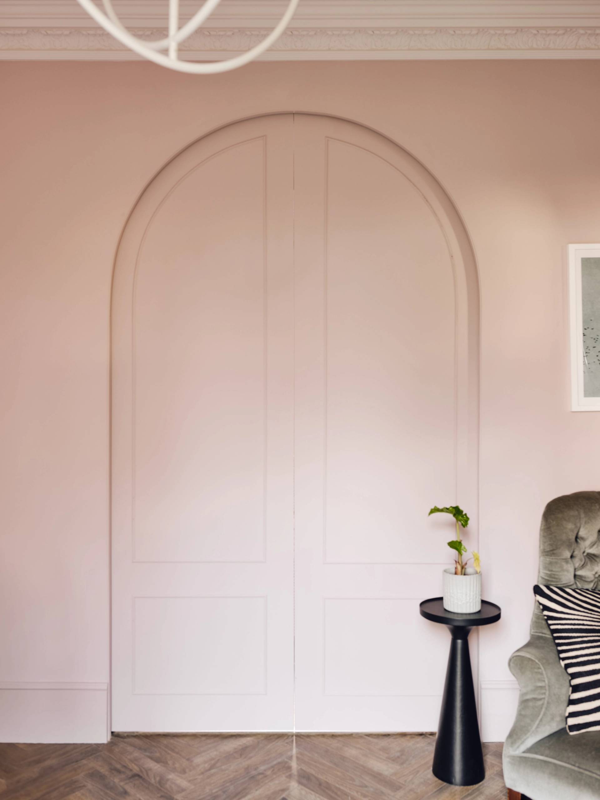 Full-height pink arch door set flush into a plaster pink wall with a small plant stand, Love Locations CR0.