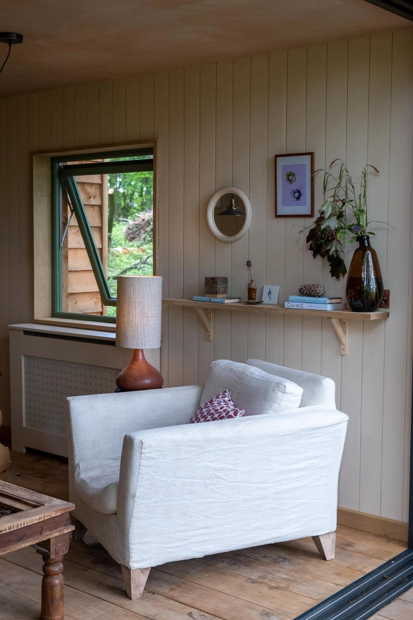 Plush white armchair positioned neatly under a minimalist wooden display shelf next to a woodland-view window, Love Locations HR4 8ls.