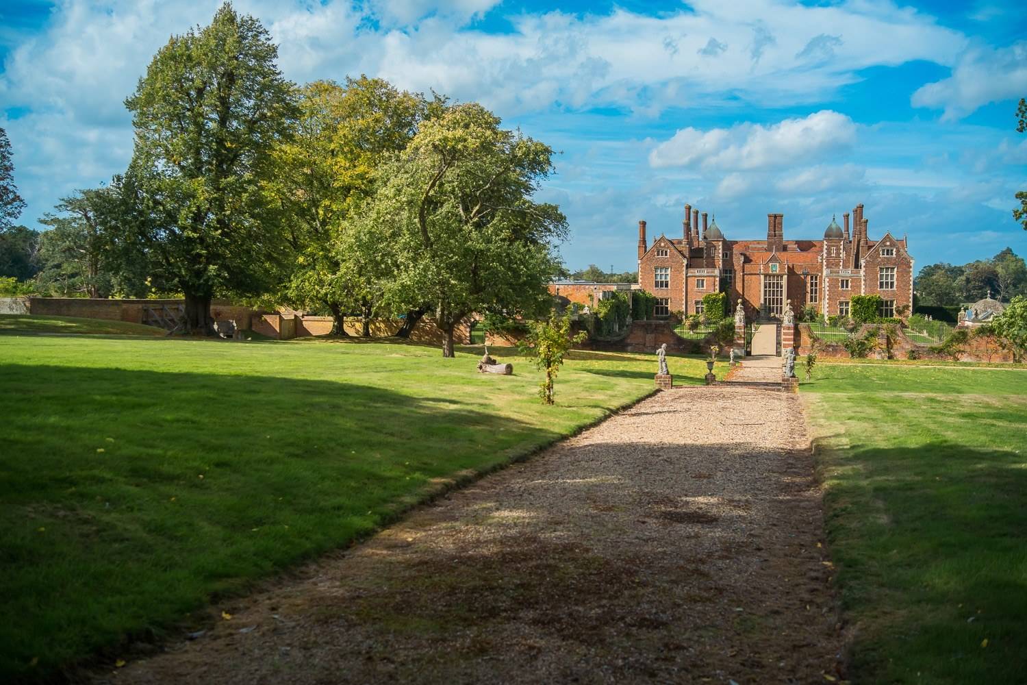 Sprawling green lawns and gravel path leading toward the historic red-brick manor house in Hertfordshire AL9 from Love Locations.