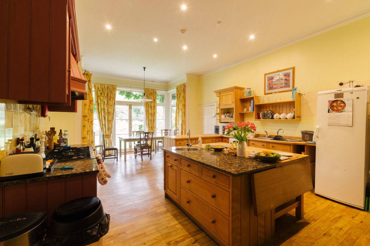 Country house kitchen dining space with oak island unit, yellow walls, and garden views through french doors, perfect for culinary ads, Love Locations SE15.
