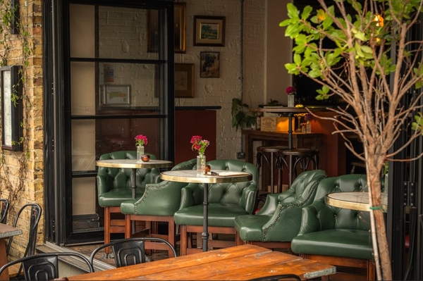 Bespoke restaurant seating booth featuring plush green leather chairs, marble-topped cocktail tables, and natural foliage accents, ideal for editorial lifestyle lookbooks, Love Locations SW16.