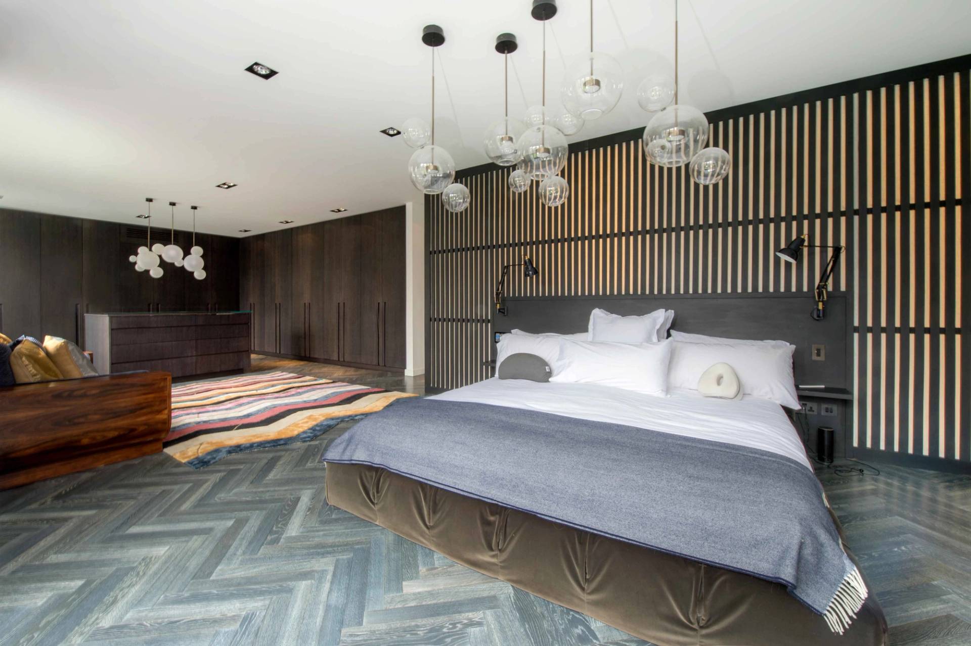 Chic master bedroom shoot location featuring a stylish upholstered bed, wooden slat wall paneling, and delicate pendant globes, Love Locations.