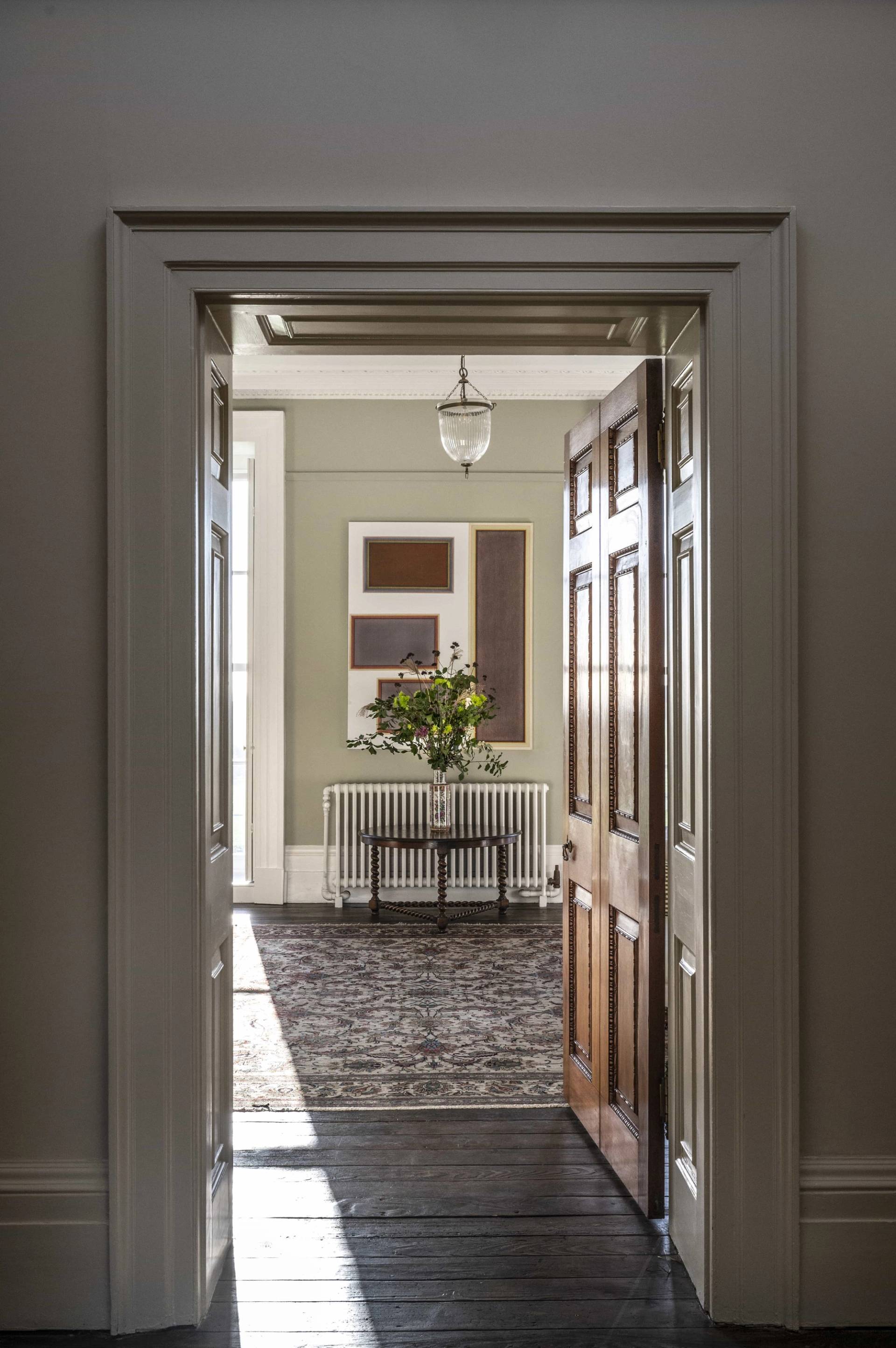 View looking through traditional double doors into a light-filled entry hallway with a console table and abstract artwork, Love Locations.
