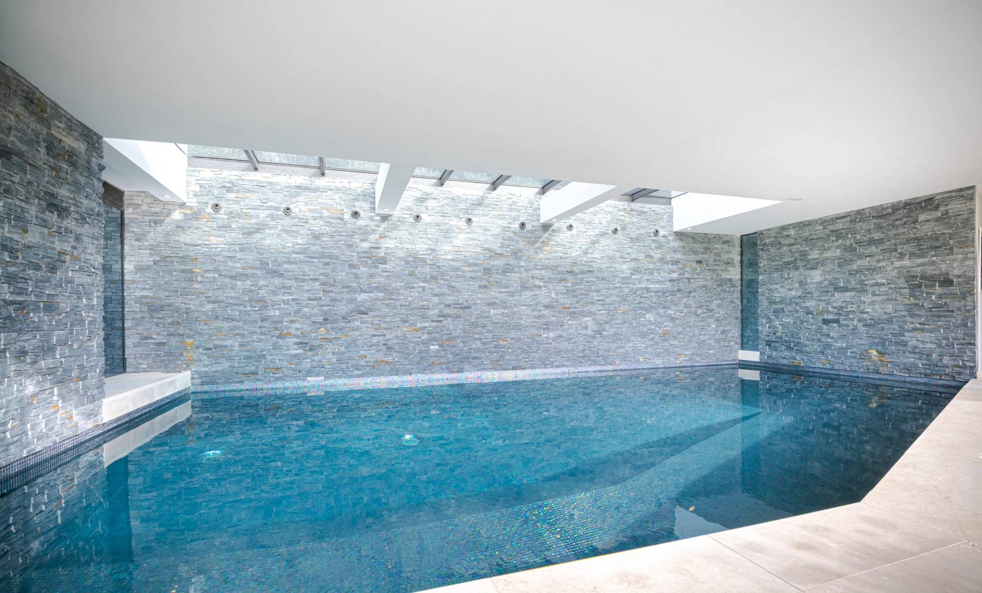 Wide-angle perspective of an indoor swimming pool room with natural skylight illumination and stone walls, Love Locations KT2.