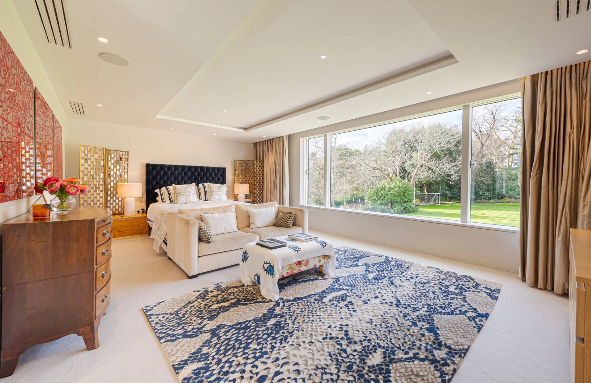 Luxury bedroom suite featuring a plush cream sofa, blue pattern rug, and floor-to-ceiling garden view windows, ideal for luxury brand ads, Love Locations KT2.