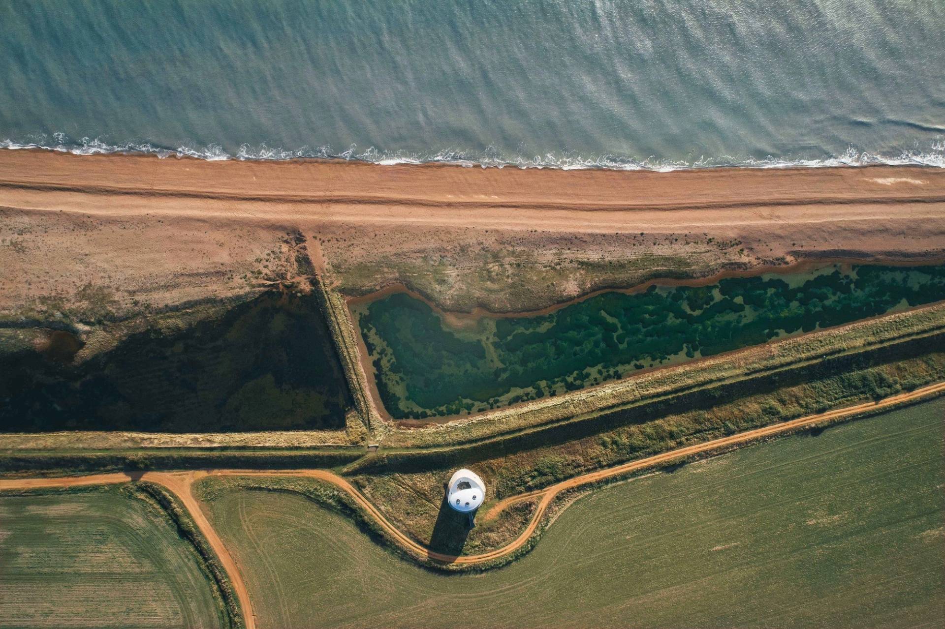 Aerial drone perspective of a coastal estuary, sea wall defenses, and countryside terrain available through Love Locations.
