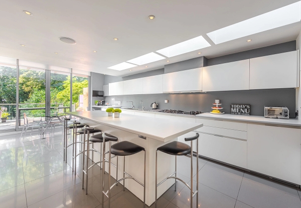 Bright minimalist white kitchen shoot location in Chiswick, London W4 featuring a large island breakfast bar and integrated skylights, ideal for high-end cooking brand commercials via Love Locations.