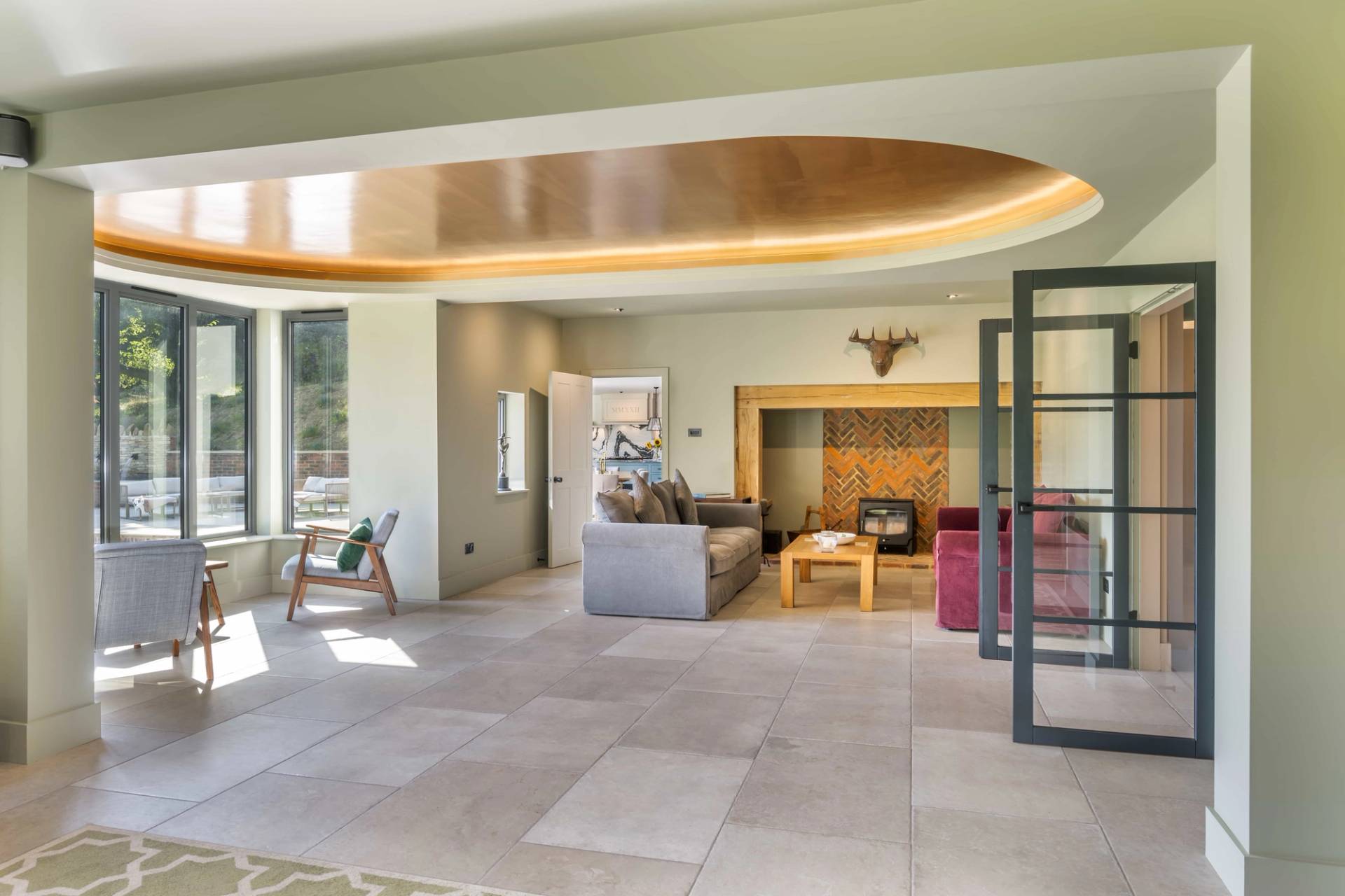 Sunlit country house lounge with stone floor tiles, log burner, and large glass windows overlooking Surrey gardens, ideal for lifestyle campaigns, Love Locations GU27.
