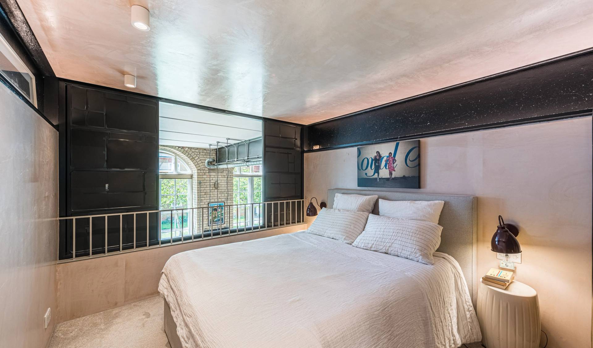 Mezzanine loft bedroom location space with a double bed looking over a safety railing onto the main living room, Love Locations.