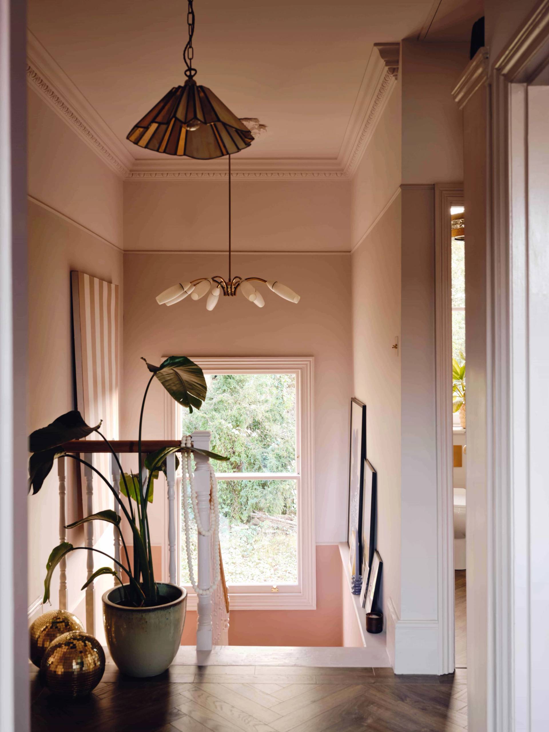 Upper landing transition with plaster pink walls, sash window view, and contemporary brass light fixture, Love Locations CR0.