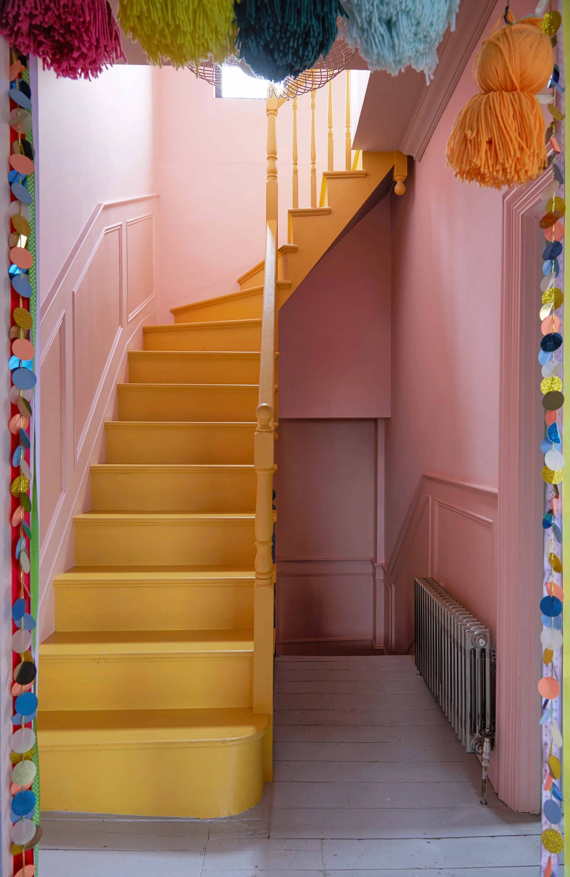 Bubblegum pink stairwell featuring bright yellow stairs and colorful paper garland decorations, Love Locations Catford.