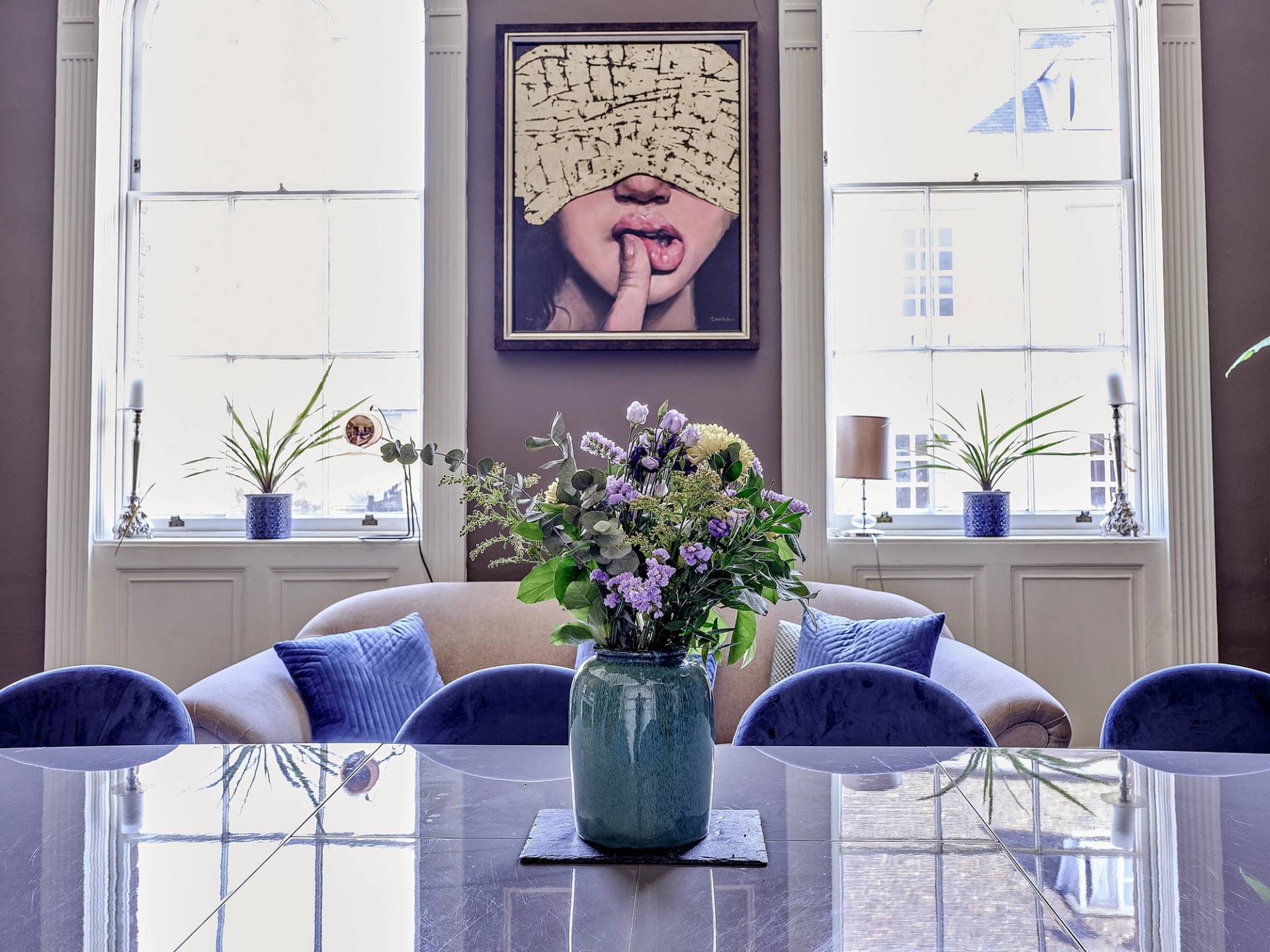 Dining room table detail set with fresh flowers and blue velvet chairs framed by sash windows, Love Locations.
