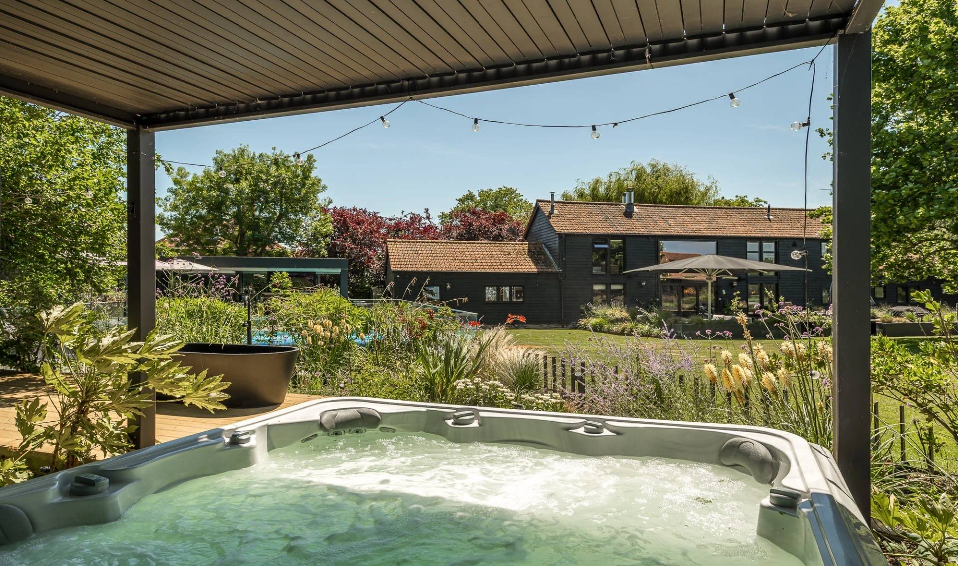 Relaxing garden hot tub location space with view towards the main luxury black weatherboard barn conversion, Love Locations.