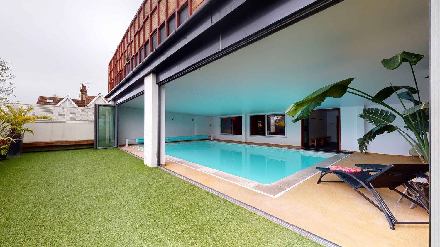 Indoor swimming pool opening directly onto an artificial grass sun terrace via full-height glass doors, Love Locations SW16.