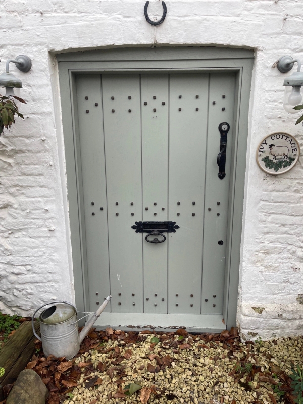 Close-up of a sage green cottage front door featuring decorative iron stud work and hardware on a historic Tudor property, Love Locations.