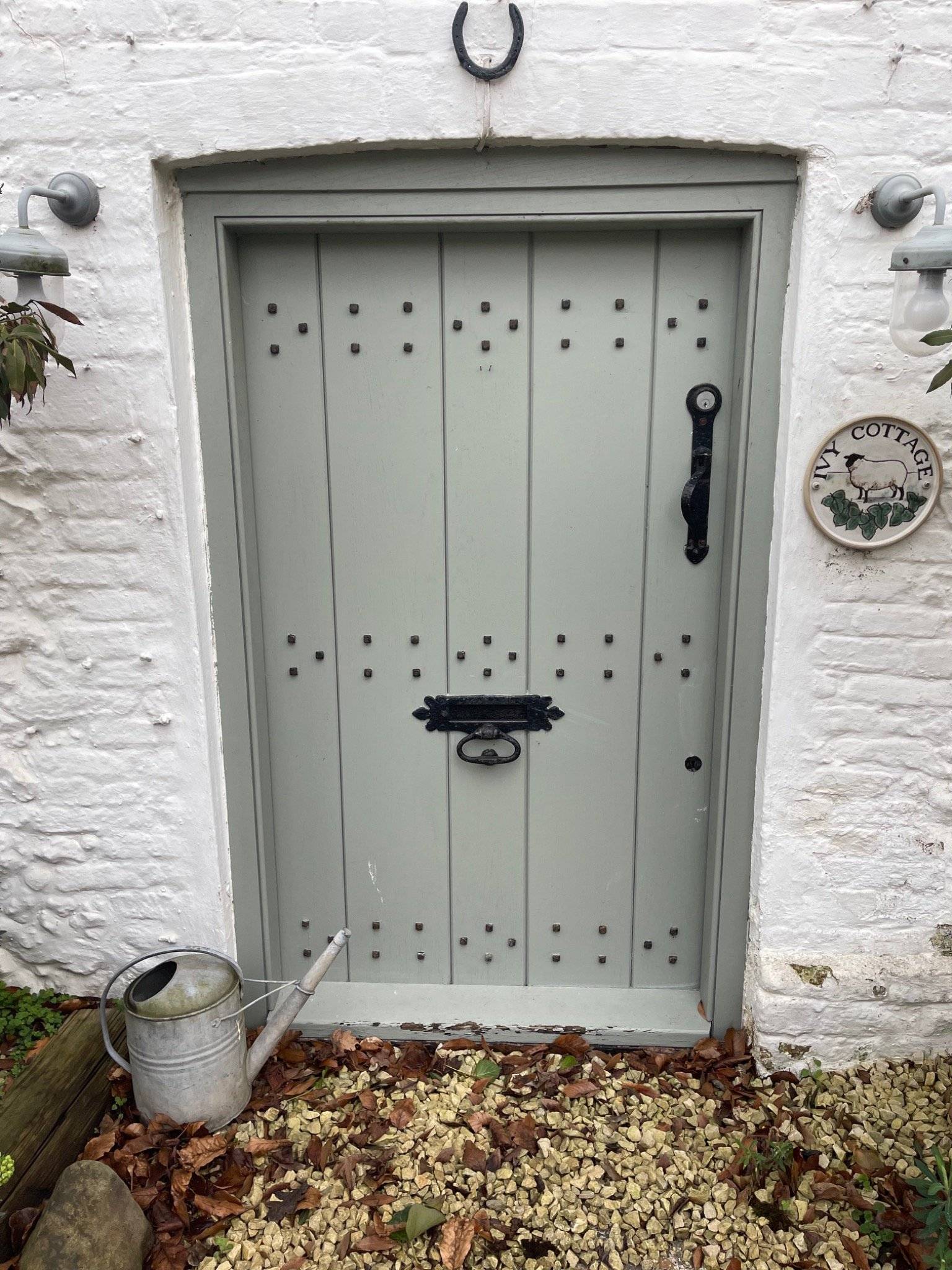 Close-up of a sage green cottage front door featuring decorative iron stud work and hardware on a historic Tudor property, Love Locations.