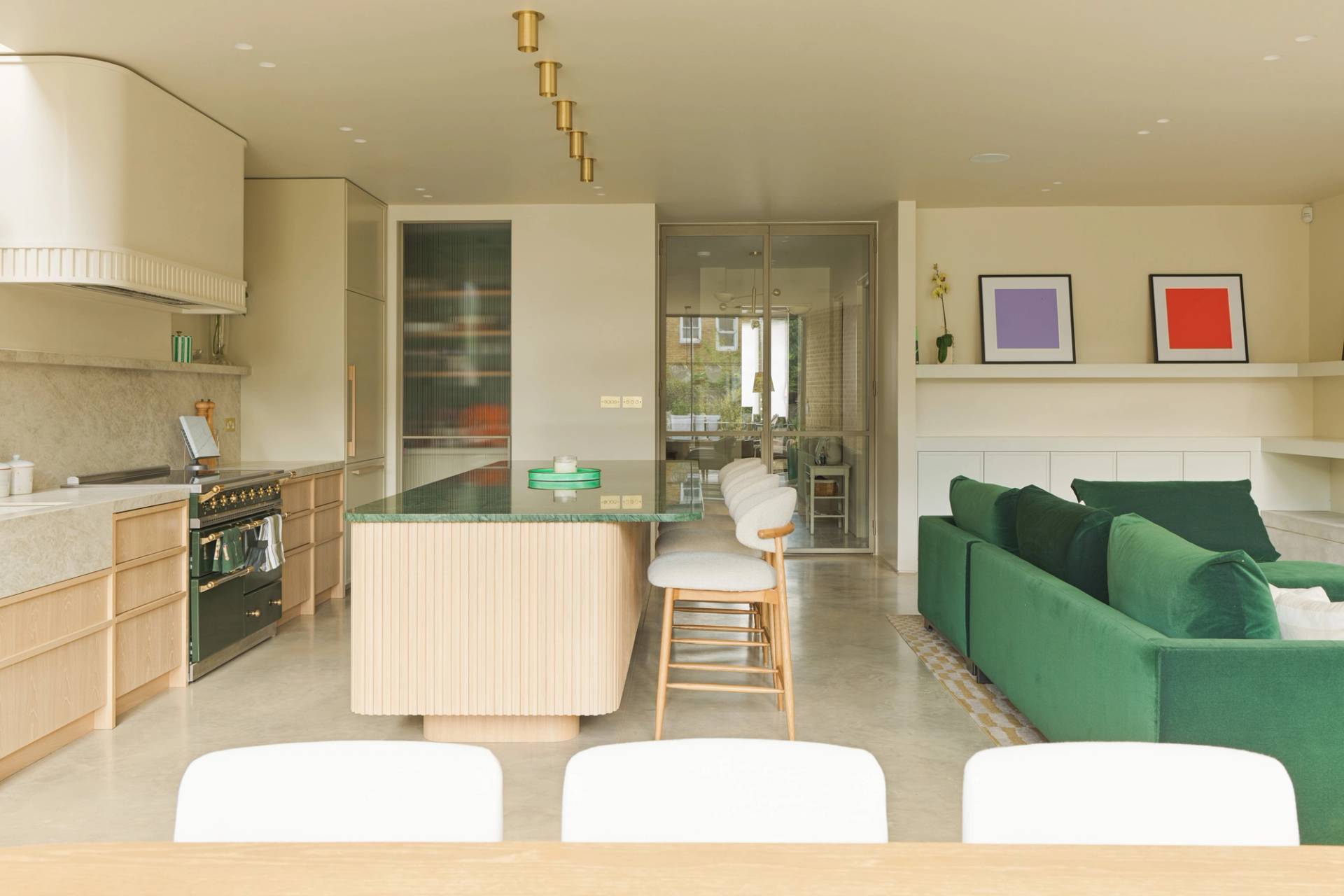 Wide interior shot of the seamless transition between kitchen, dining, and green sofa living areas by Love Locations.