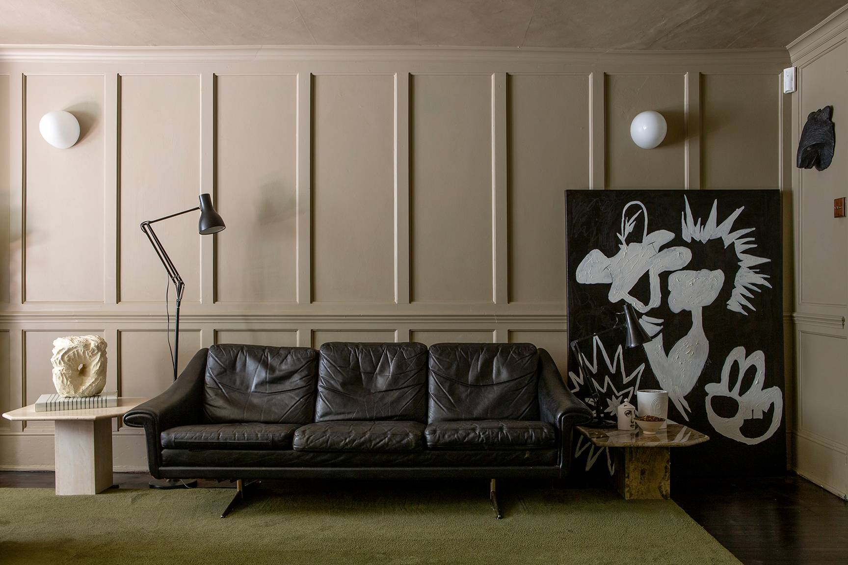 Eclectic period house location in Faversham, ME13 featuring grey wall panelling, black leather sofa, and green carpet via Love Locations.