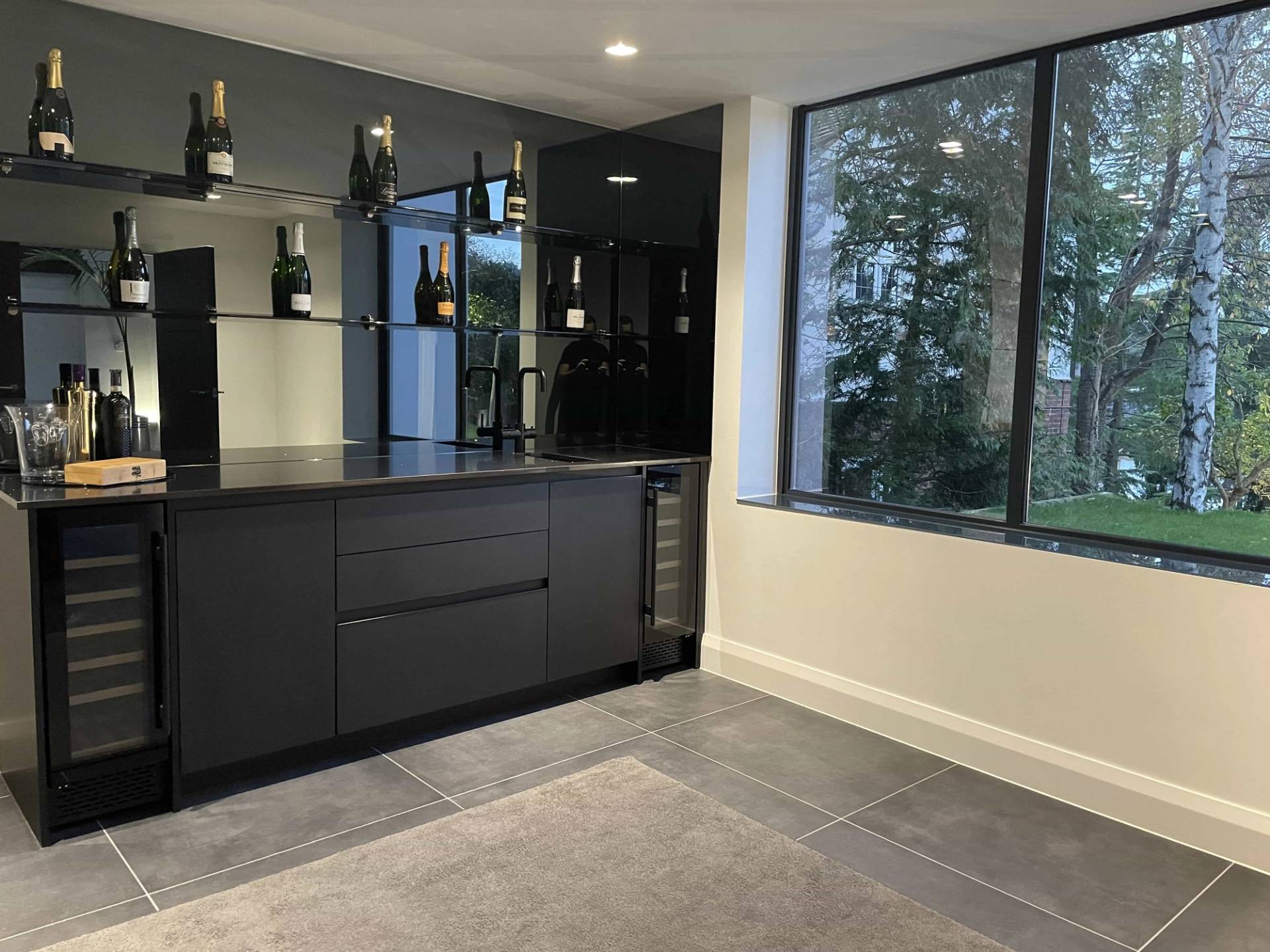 Private luxury home bar suite in Loughton, IG10 featuring sleek black cabinetry, integrated wine fridges, and backlit display shelving, ideal for commercial beverage shoots via Love Locations.