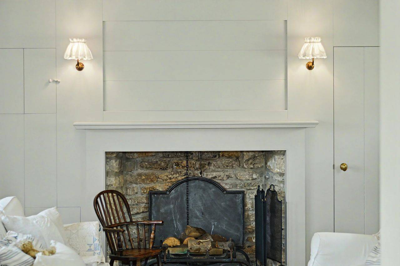 Traditional stone fireplace feature in a Cotswold cottage location house in Gloucestershire GL7 through Love Locations, with wrought-iron fire screen and wall sconce lighting.