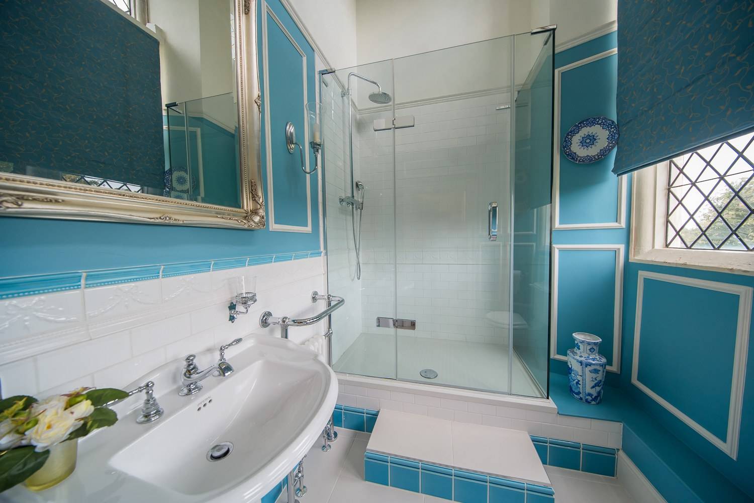 Bright blue and white period bathroom location house featuring a glass walk-in shower and pedestal sink through Love Locations.